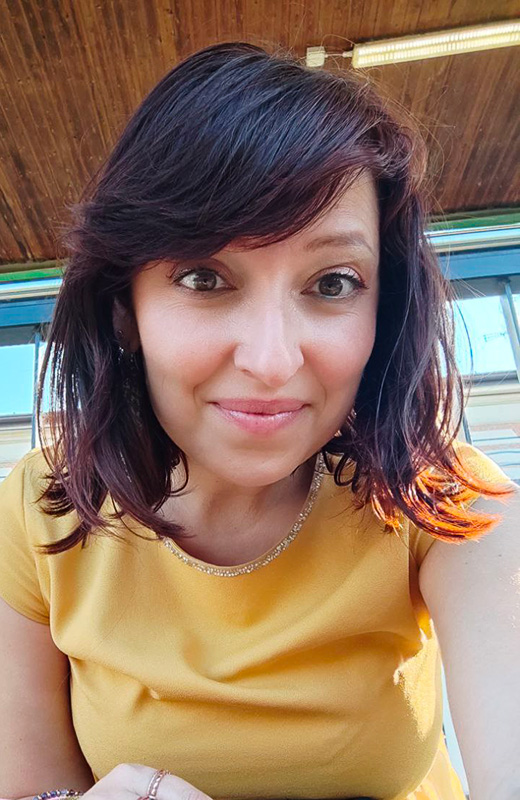 Selfie di Elena con una maglietta giallo polenta, sullo sfondo una stazione